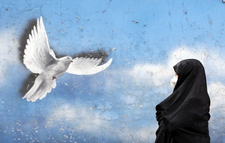 Woman in a chador walks past a mural of a peace dove in Tehran, November 2020.